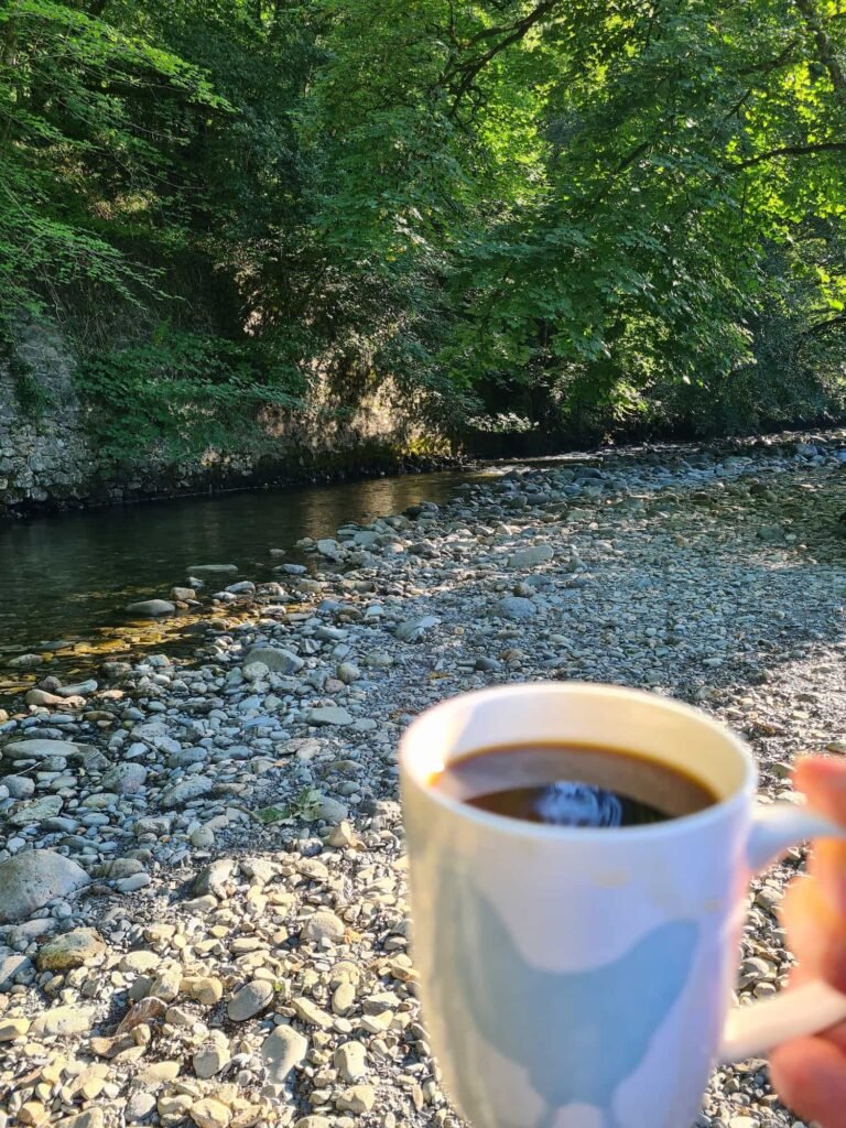 A cup of coffee in the foreground with a river bd behind