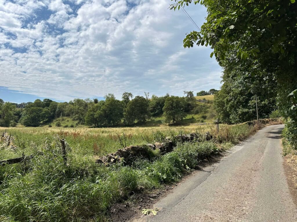 A wide view, with a footpath post leading over a wall